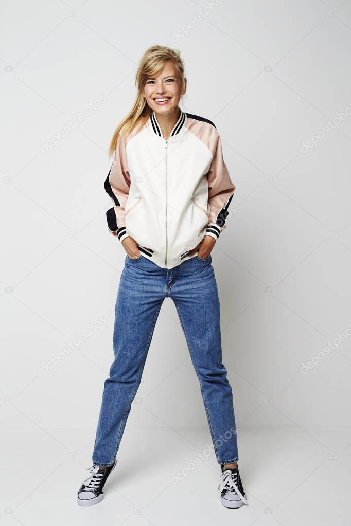 Girl wearing jeans and jacket standing and smiling at camera