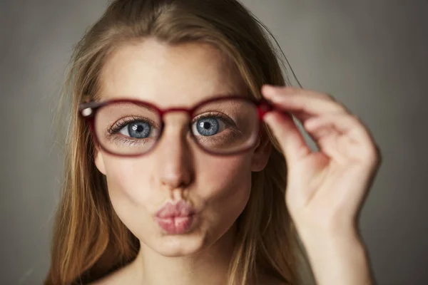 Portrait of woman with big blue eyes holding glasses blowing a kiss at camera