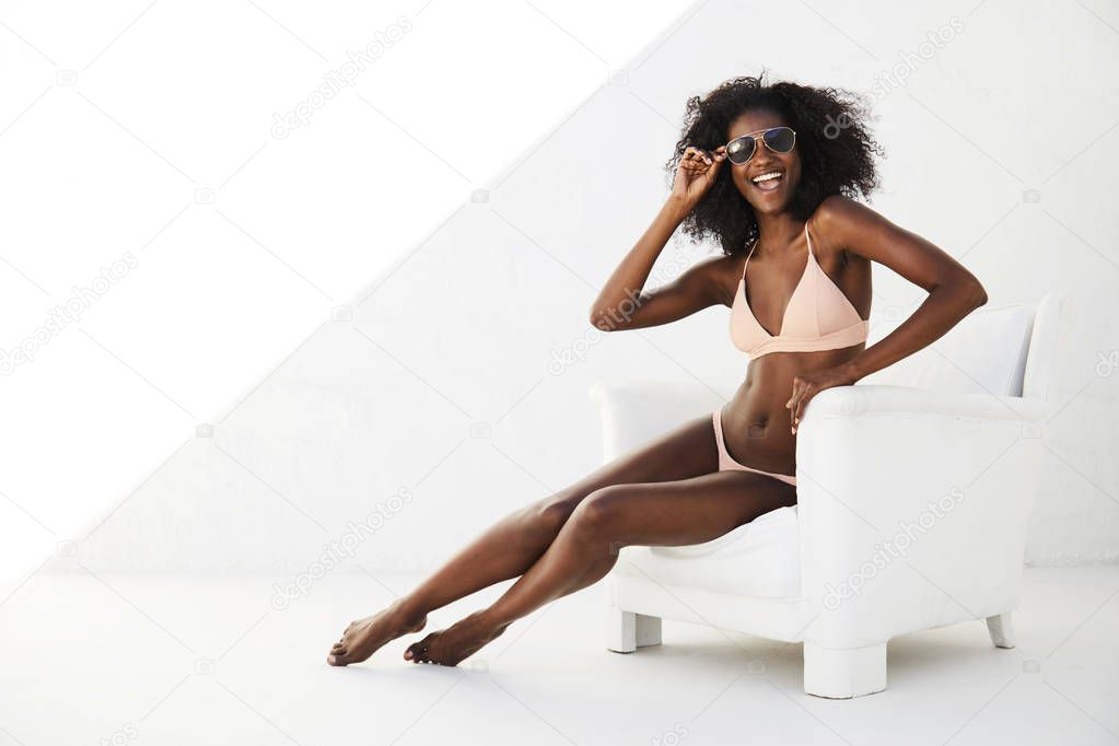 Young african woman in bikini and shades, sitting in armchair