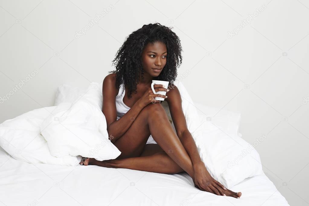 young african woman with coffee cup in bed, looking aside