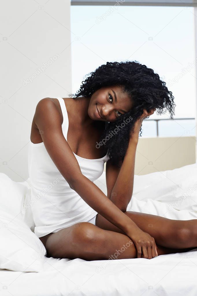 Young african girl sitting in bed posing, smiling to camera