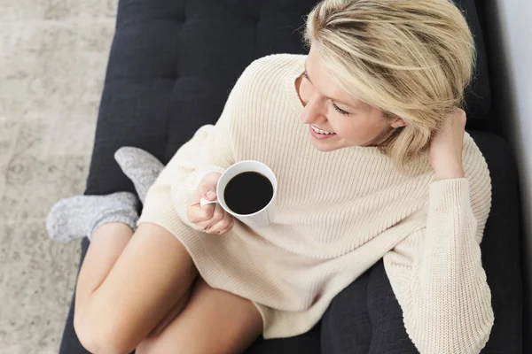 Blond woman relaxing on sofa with coffee cup, overhead view