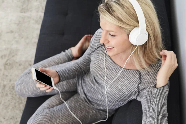 Woman in headphones with smartphone on sofa