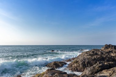 Kaya ve okyanus. Güneşli bir günde, yaz denizi boyunca mavi gökyüzünde bulutları kaplayan kaya plajı..