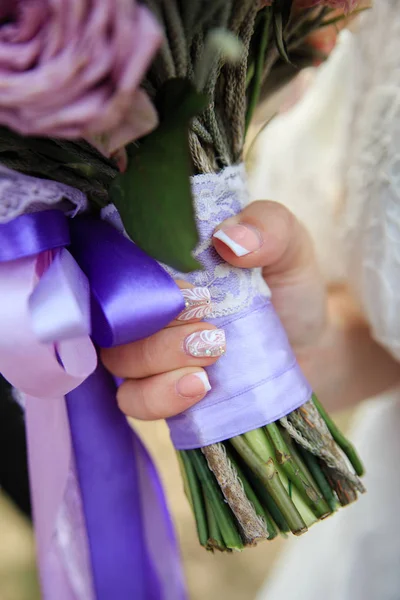 Manikür ile gelin eli sıkıca bir Lila şeritler ile bağlı düğün buket sıkıştırır