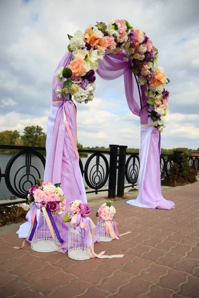 Свадебная церемония на берегу реки с фиолетовыми лентами и клеткой для птиц — стоковое фото