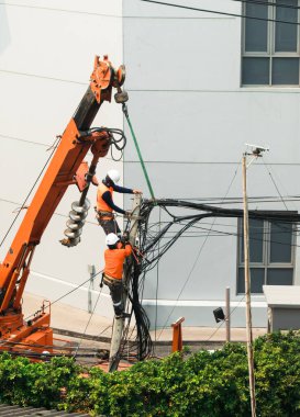 Elektrikçiler elektrik hatlarını kurmak ve onarmak için turuncu renkli vinçle elektrik direklerine tırmanıyorlar..
