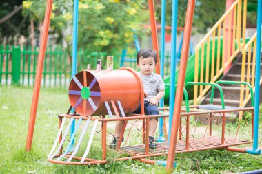 Genç Asyalı çocuk oyun bahçesi und sallanan bir demir tren