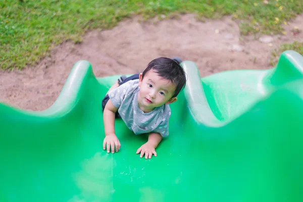 Малыш-азиат забирается на горку на игровой площадке в сумме — стоковое фото