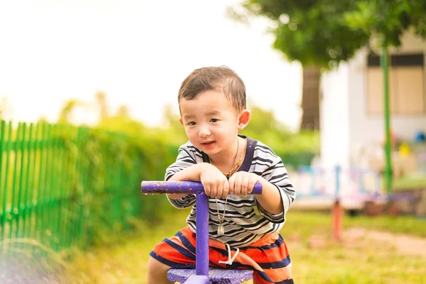 Asian kid riding seesaw board at the playground under sunlight, — Stock Photo, Image