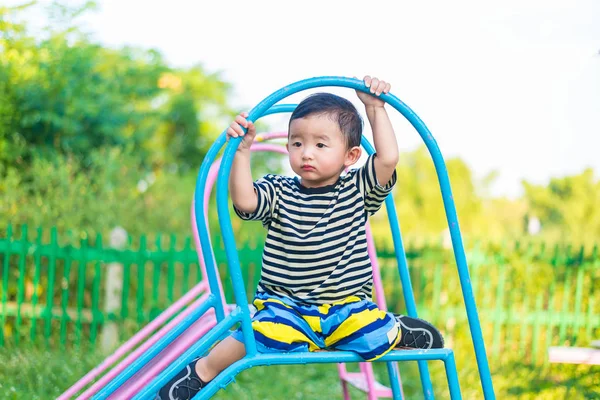 Triste niño asiático sentado en diapositiva en el patio de recreo en el d — Foto de Stock