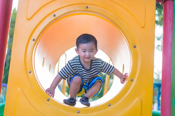 Söta asiatiska pojken spelar och leende i gula tunneln på lekplat — Stockfoto