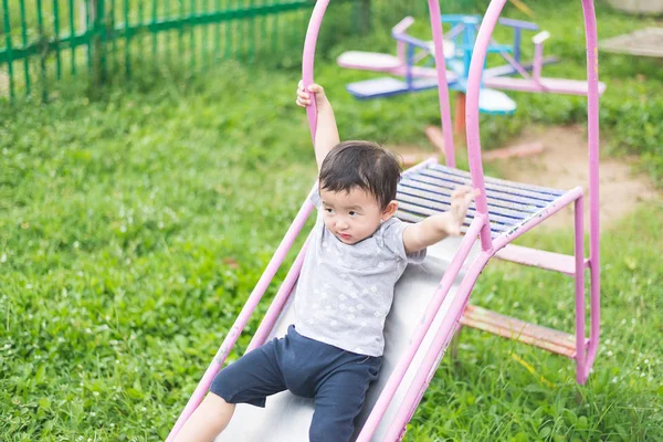 Kleines asiatisches Kind spielt Rutsche auf dem Spielplatz unter der Sonne — Stockfoto