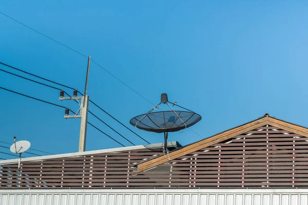 Große schwarze Satellitenschüssel auf dem Dach mit blauem Himmel. — Stockfoto
