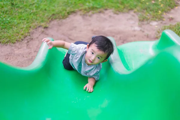 Little Asian kid climbing up the slide at the playground in summ — Stock Photo, Image