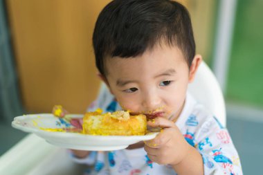 Asyalı çocuk yüzünde doğum günü pastası ile krem yeme.