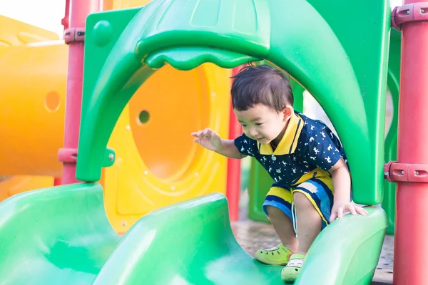Pequeño niño asiático jugando diapositiva en el patio de recreo bajo el sunli — Foto de Stock