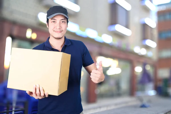 Asiático entrega hombre pulgares arriba con cartulina caja en borrosa espalda — Foto de Stock