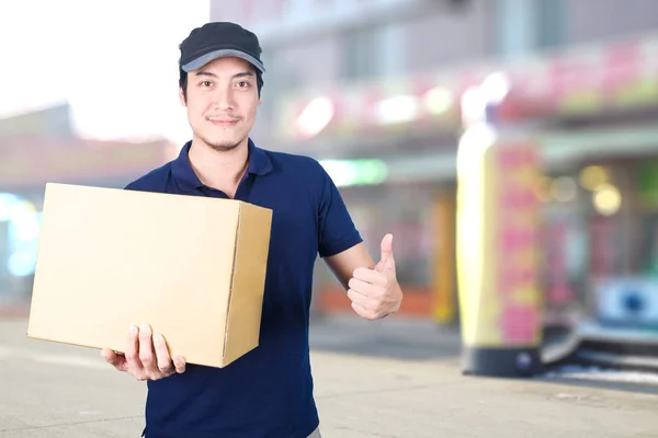 Asiático entrega hombre pulgares arriba con cartulina caja en borrosa espalda — Foto de Stock