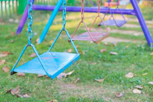 Empty chain and metal swings in playground and meadow grass fiel