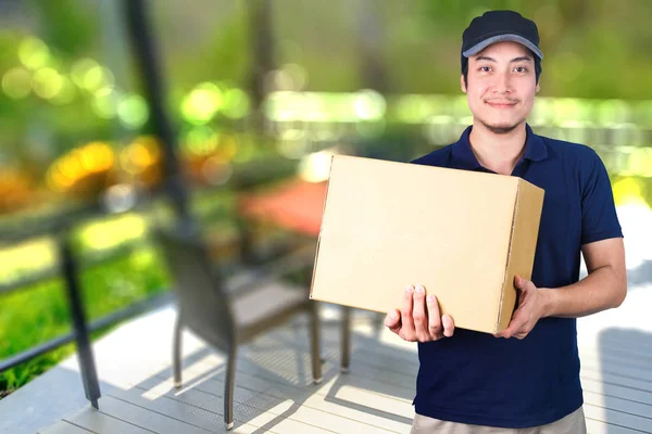 Asiático sorriso Entrega homem com caixa de papelão na mão de pé em — Fotografia de Stock