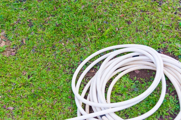 Gartenschlauch oder weißer Gummischlauch mit Wasserhahn auf dem Rasenplatz. — Stockfoto
