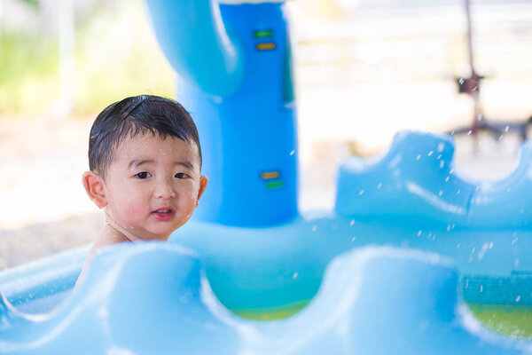 Asian kid playing in inflatable baby swimming pool on hot summer
