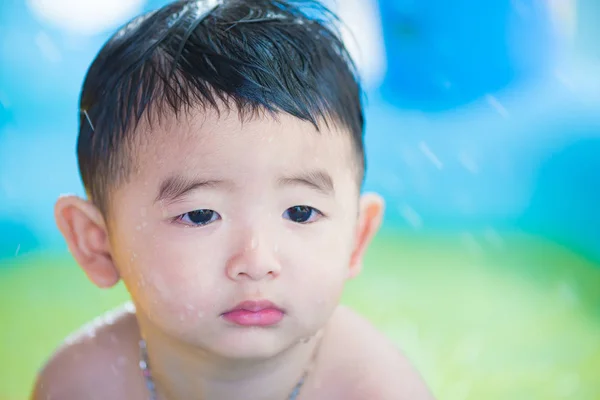 Sad Asian kid playing alone in inflatable baby pool.