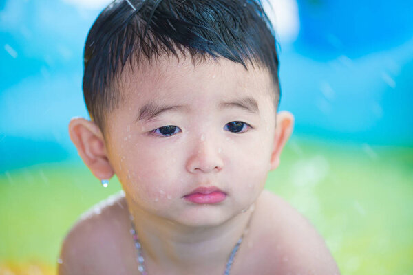 Sad Asian kid playing alone in inflatable baby pool.