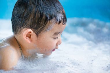 Asyalı çocuk su ve köpük ile oynarken şişme bebek havuzu üzerinde