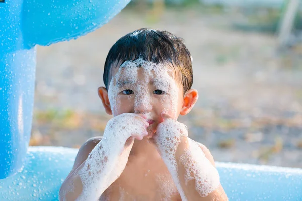 Asian boy playing with water and foam in inflatable baby pool on — Stock Photo, Image