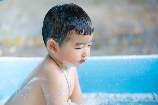 Menino asiático brincando com água e espuma na piscina inflável do bebê no — Fotografia de Stock