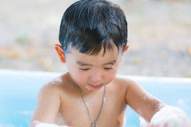 Asyalı çocuk su ve köpük ile oynarken şişme bebek havuzu üzerinde