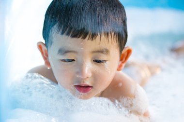 Asyalı çocuk su ve köpük ile oynarken şişme bebek havuzu üzerinde