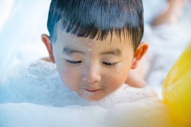 Asyalı çocuk su ve köpük ile oynarken şişme bebek havuzu üzerinde