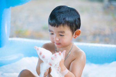 Asyalı çocuk su ve köpük ile oynarken şişme bebek havuzu üzerinde