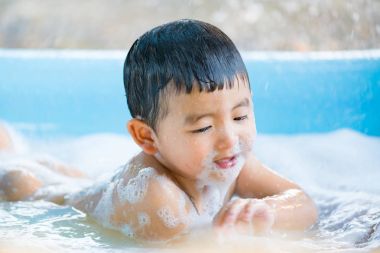 Asyalı çocuk su ve köpük ile oynarken şişme bebek havuzu üzerinde