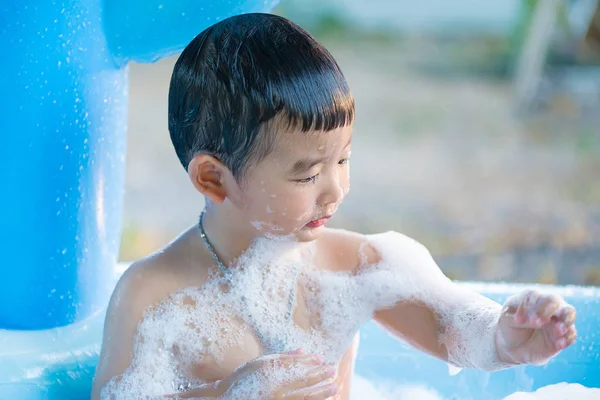 Menino asiático brincando com água e espuma na piscina inflável do bebê no — Fotografia de Stock