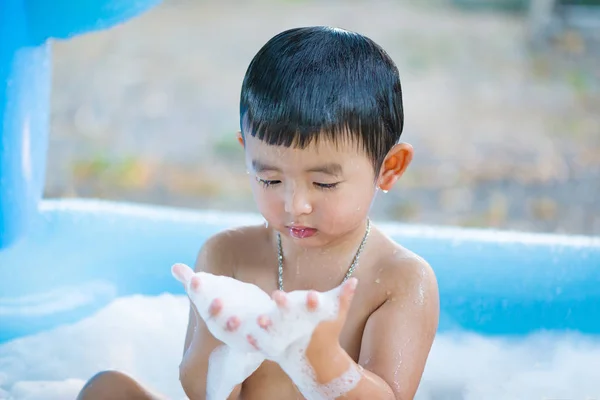 Menino asiático brincando com água e espuma na piscina inflável do bebê no — Fotografia de Stock