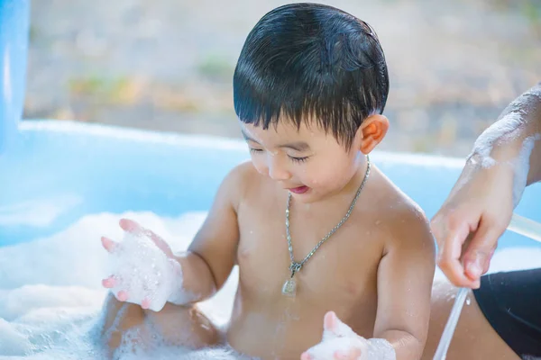 Aasian poika leikkii vedellä ja vaahdolla puhallettavassa vauvan uima-altaassa — kuvapankkivalokuva