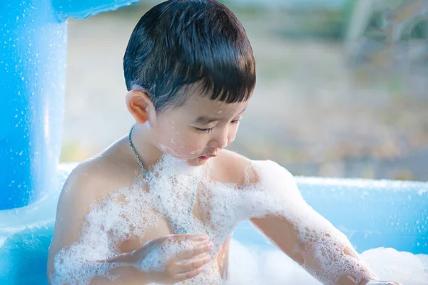Asian boy playing with water and foam in inflatable baby pool on — Stock Photo, Image
