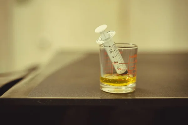 Seringa com xarope de medicamento em um copo farmacêutico de medição — Fotografia de Stock