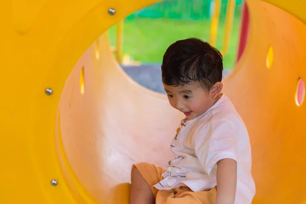 Lindo asiático chico jugando y sonriendo en amarillo túnel en el playg — Foto de Stock