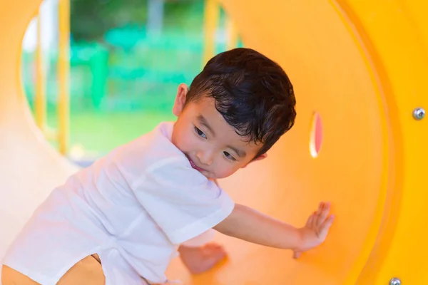 Söta asiatiska pojken spelar och leende i gula tunneln på lekplat — Stockfoto