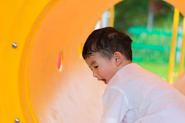 Lindo asiático chico jugando y sonriendo en amarillo túnel en el playg — Foto de Stock