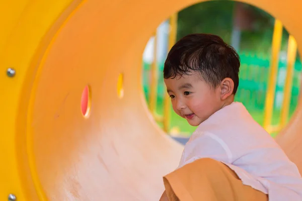 Lindo asiático chico jugando y sonriendo en amarillo túnel en el playg — Foto de Stock