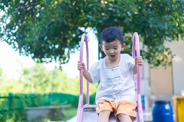 Pequeño niño asiático jugando diapositiva en el patio de recreo bajo el sunli — Foto de Stock