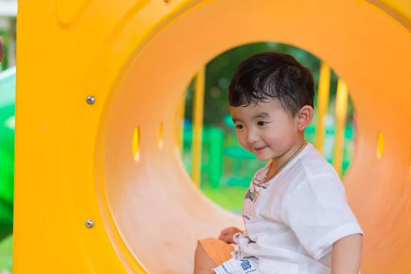 Lindo asiático chico jugando y sonriendo en amarillo túnel en el playg — Foto de Stock