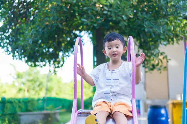 Little Asian kid playing slide at the playground under the sunli — Stock Photo, Image