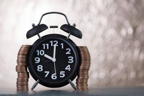 Reloj despertador y pilas de moneda en la mesa de trabajo, tiempo de ahorro — Foto de Stock